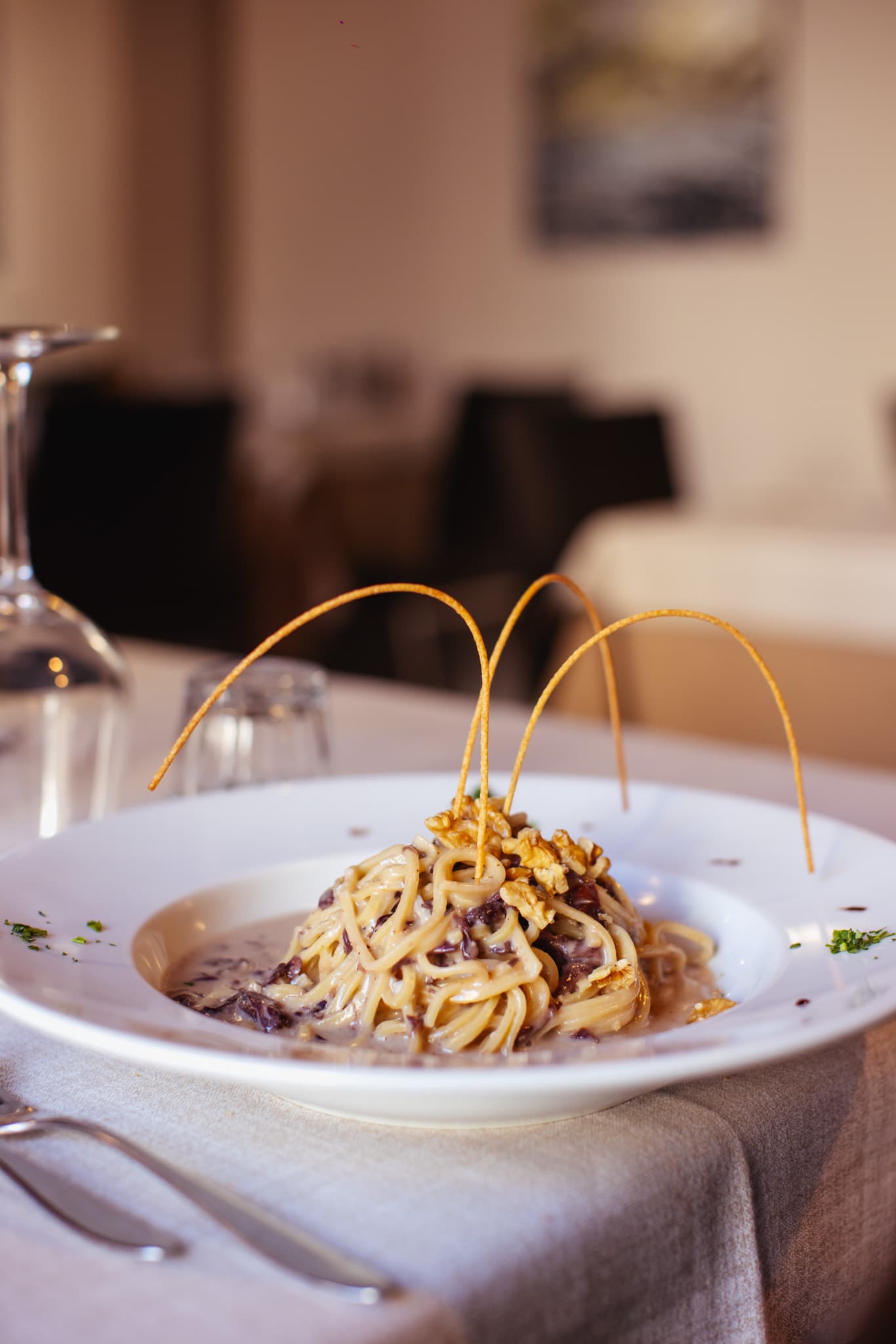 Elegant pasta with creamy sauce, walnuts, and crispy garnish on a restaurant table.