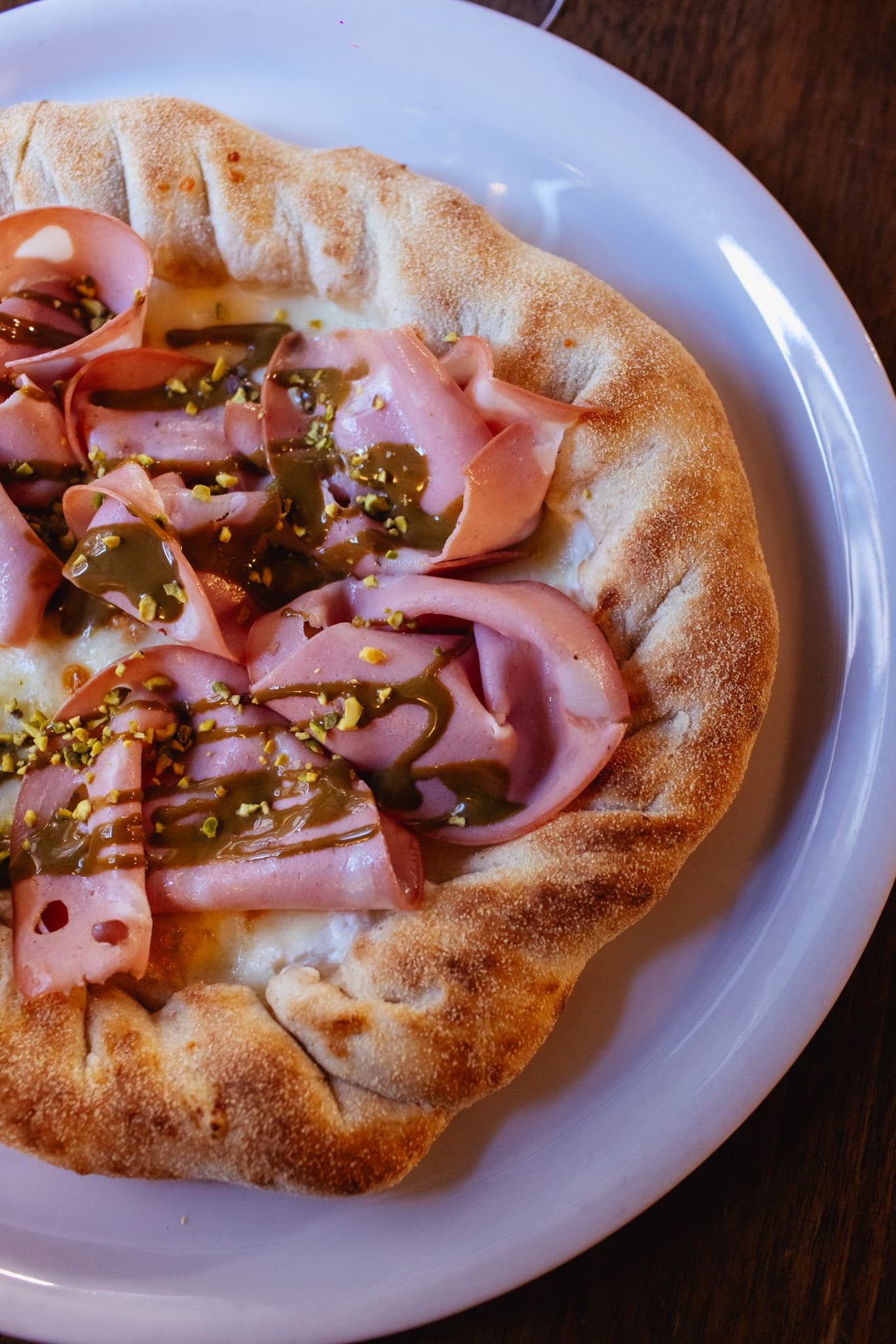 Neapolitan-style pizza with mortadella, pistachio cream drizzle, and chopped pistachios.